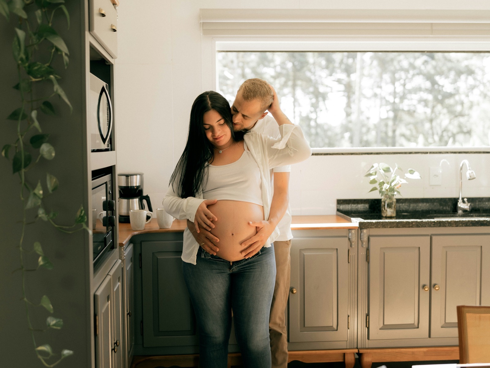 Expectant parents stand together in their kitchen with their hands on the baby bump