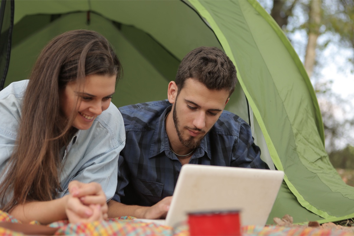 Couple sitting by a tent and looking at a laptop together